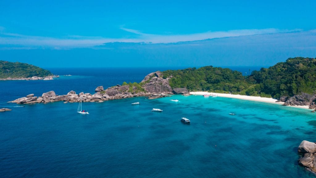 Aerial view of a Similan island with granite boulders, a white sand beach and boats moored in turquoise water