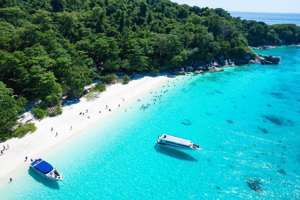 Aerial view of a white-sand beach and turquoise bay in the Similan Islands with speedboats moored offshore