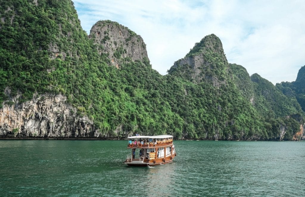 Big wooden tour boat cruising between towering green limestone karsts in Phang Nga Bay