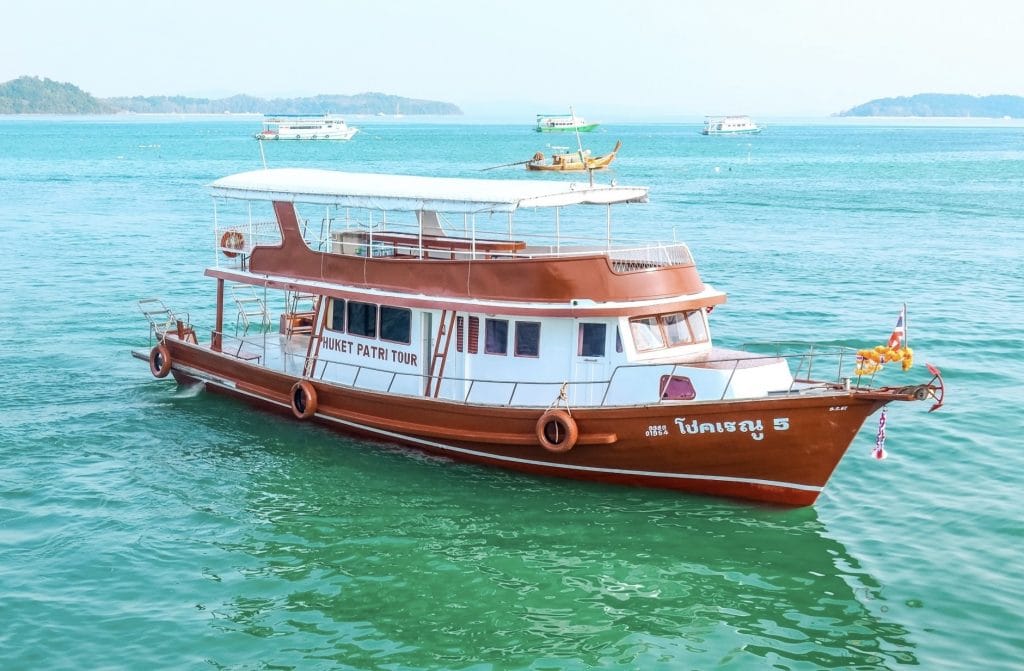 Traditional big wooden tour boat with an orange hull cruising on turquoise water in Phang Nga Bay