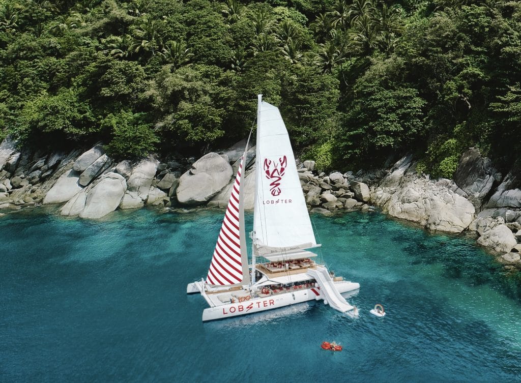 Sailing catamaran anchored by granite boulders and clear water off Racha Yai island near Phuket
