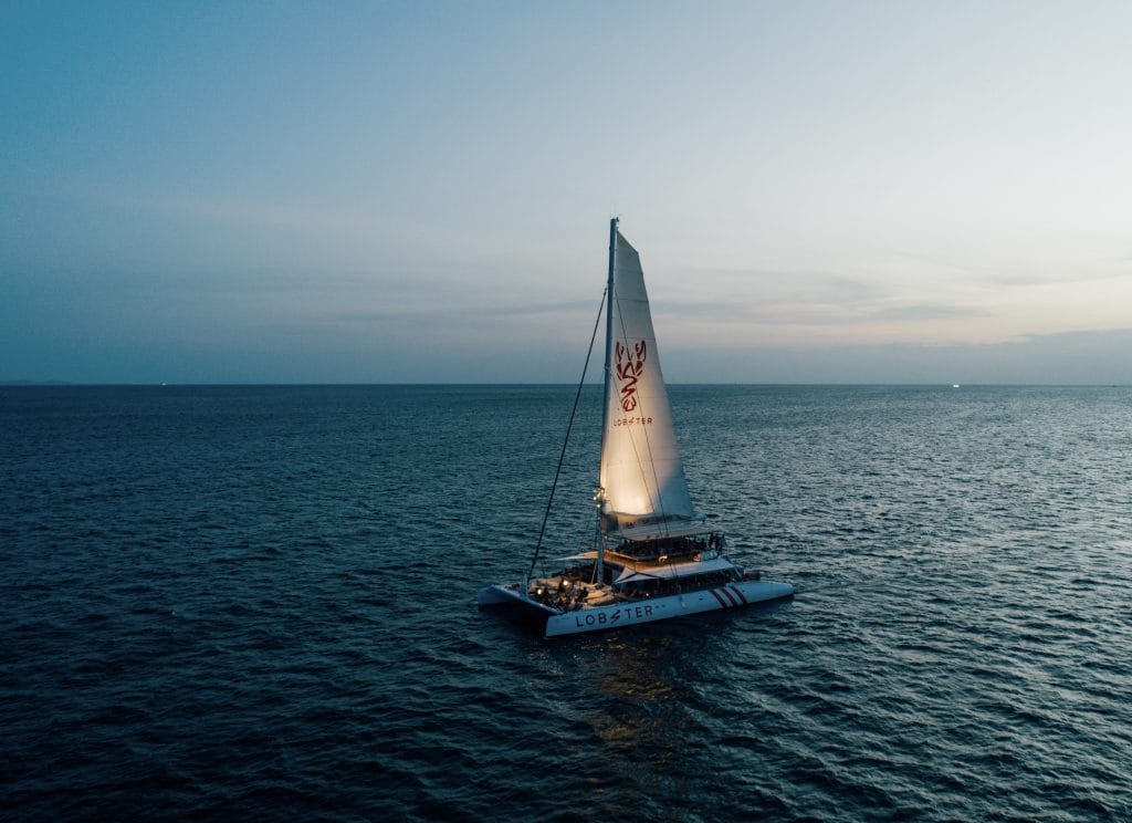 Sailing catamaran with its sail up crossing a calm sea off Phuket in soft evening light